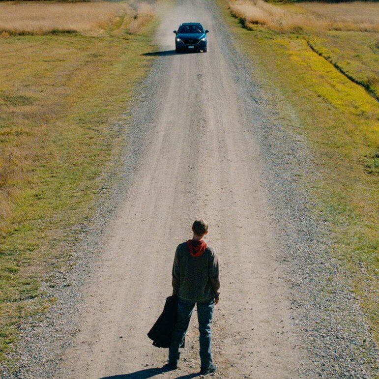 Person walking alone on a gravel road towards a car in the distance.